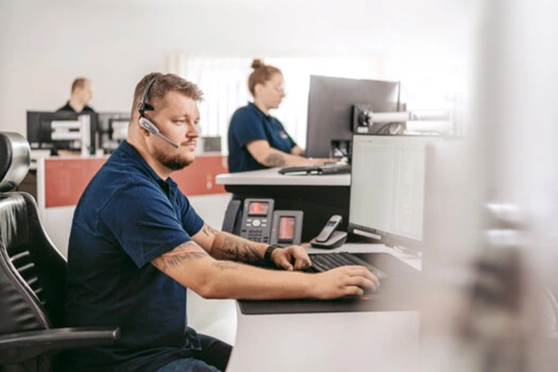 Dussmann Mitarbeiter trägt Headset und arbeitet am Computer. 