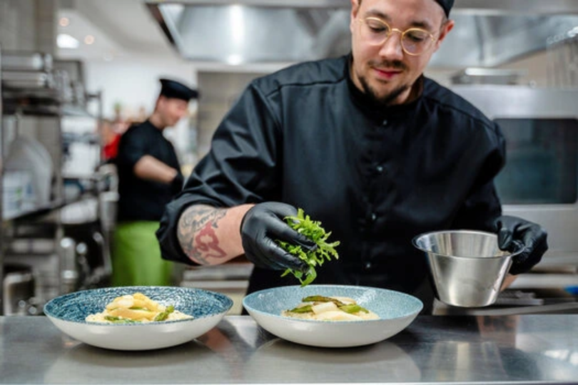 Dussmann Food Services Mitarbeiter belegt Essen mit Rucola. 