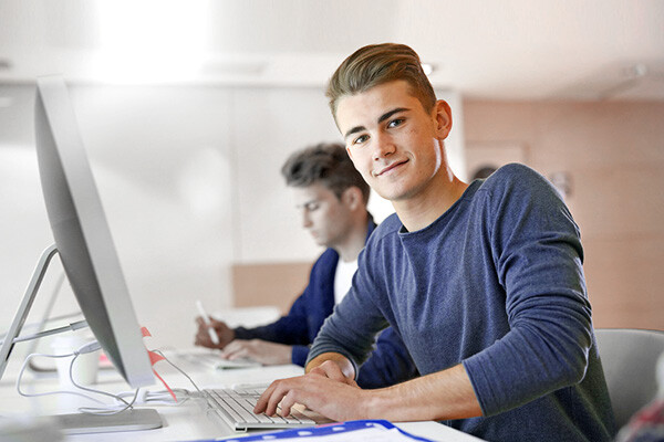 Dussmann-Mitarbeiter, der an einem Schreibtisch am Computer sitzt und lächelt.